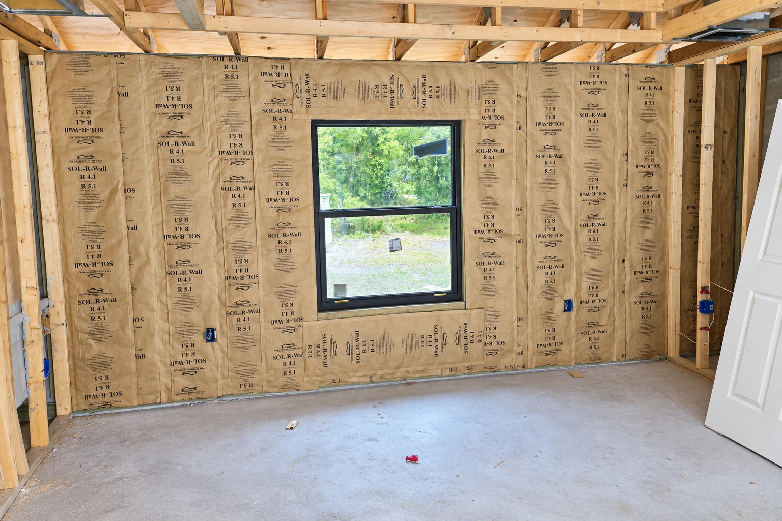 Unfinished room with kraft-faced insulation fitted between exposed wooden wall studs and a window.