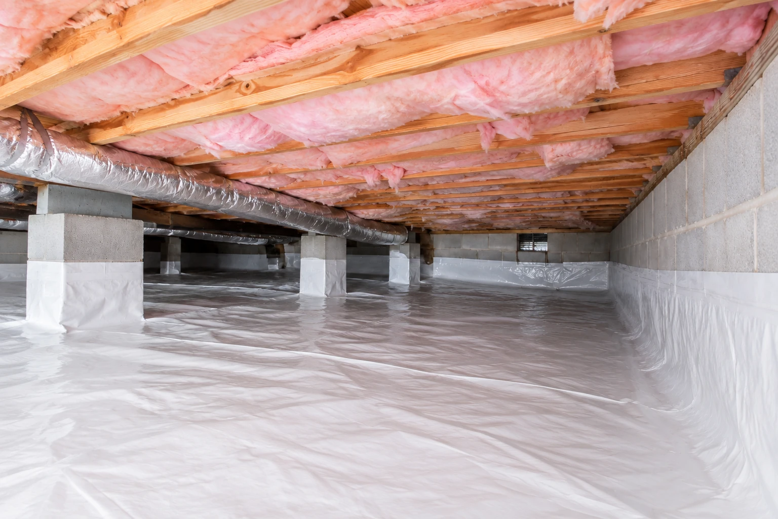 Pink batt insulation lines the underside of a crawl space floor above a plastic vapor barrier and wrapped support piers.